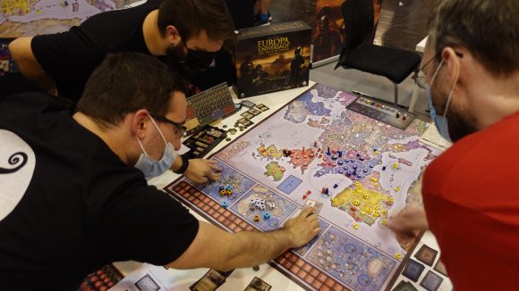 Europa Universalis board game release date several people playing the game, while pointing to tokens on its board