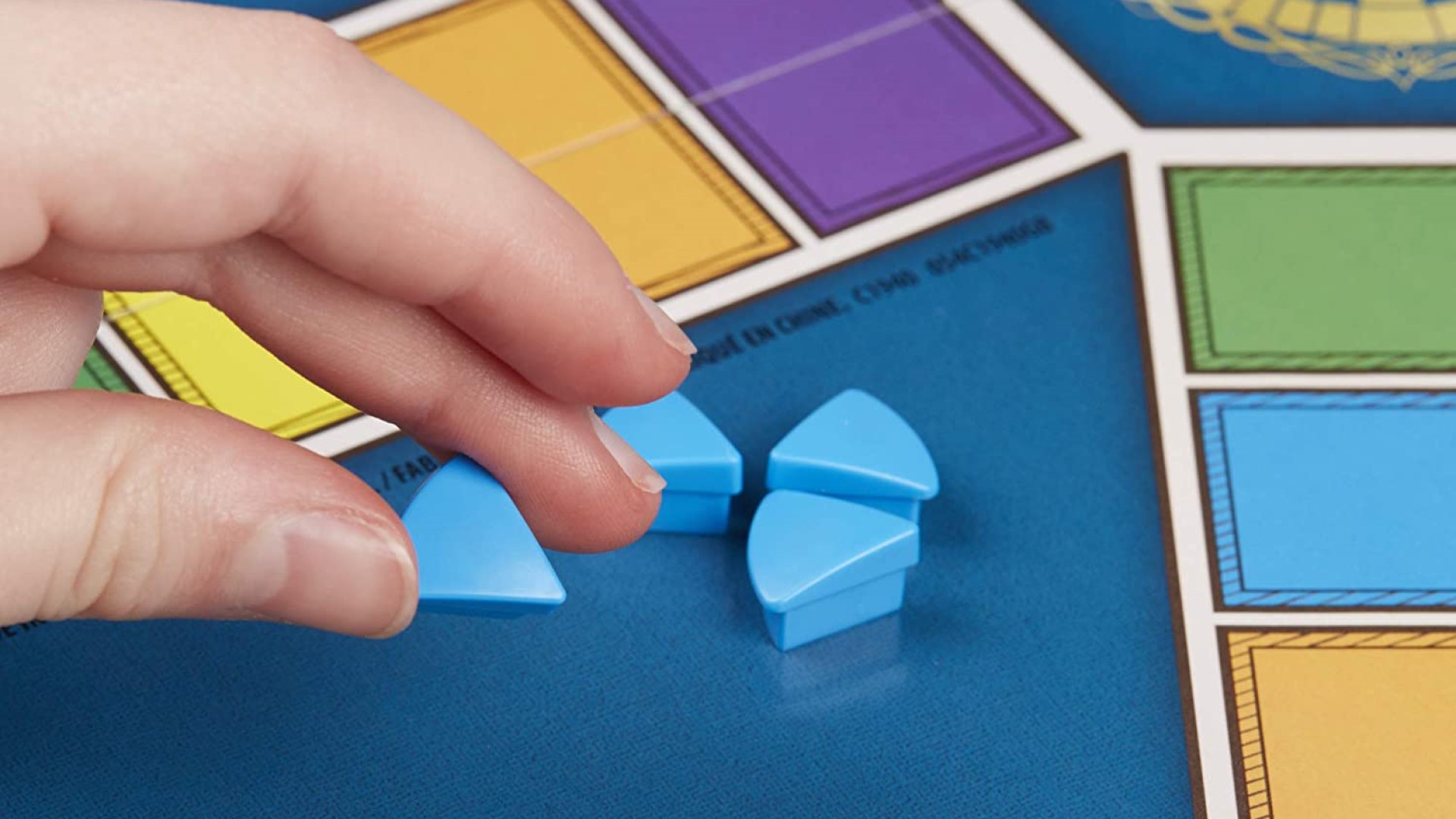Best classic board games: Trivial Pursuit. Image shows a a hand reaching over a Trivial Pursuit board for some light blue segment pieces.