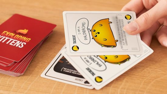 Best drinking board games guide - Exploding Kittens sales photo showing a hand playing down cards next to the EK deck