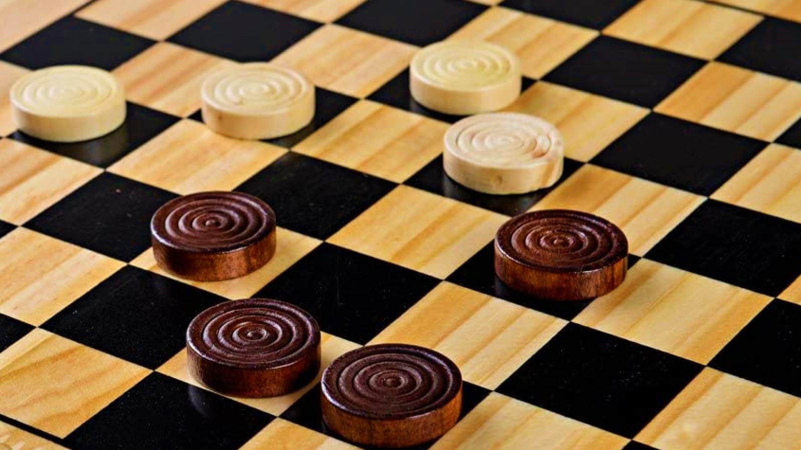 How to play checkers - a closeup of a wooden checkerboard, with four white and four brown pieces scattered on top