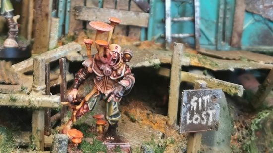 Warhammer 40k Necromunda: Photo from Sumphulk of a model by Alastair Fleming, a fungus-infected underhive mutant in a shanty town beside a sign that reads "git lost"