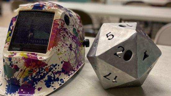 DnD dice - a giant metal d20 beside a machine used to create it.