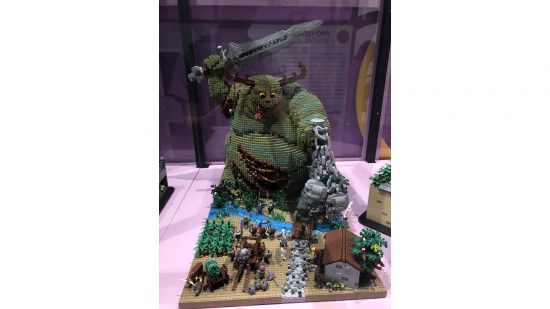 Warhammer 40k a great unclean one made of lego, attacking a medieval village with tiny minifigures putting up a doomed defense