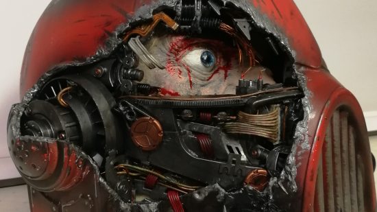 Warhammer 40k Space Marine helmet sculpted by Florian Kschonek - a red helmet with extensive damage on the right side, revealing metal components and a human face