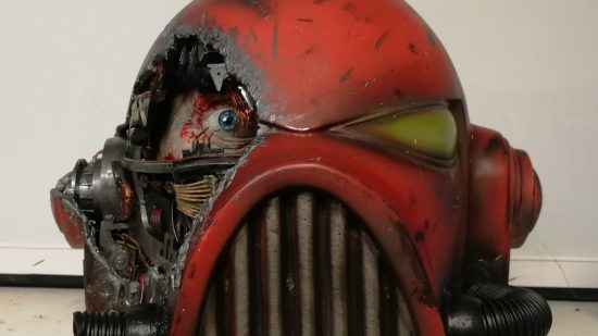 Warhammer 40k Space Marine helmet sculpted by Florian Kschonek - a red helmet with one yellow eye lens, a steel mouth grille, and damage on the right side exposing wiring and a human face