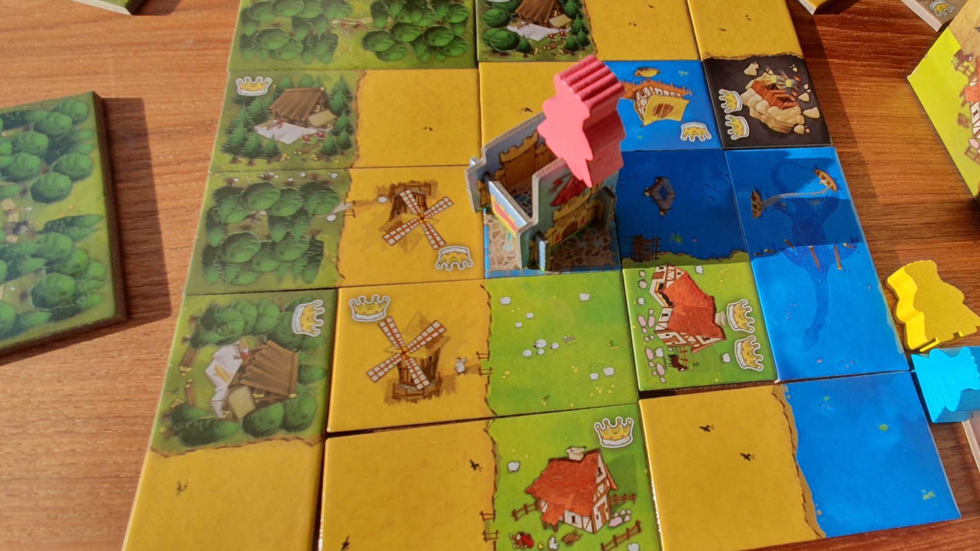 Kingdomino review - photo of a complete kingdom made from landscape domino tiles, in the center is cardboard castle, with a pink meeple balanced on top