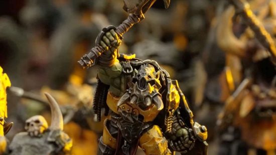 Warhammer Age of Sigmar Orruk Ardboy - action shot of a model by Games Workshop, a hulkin Ork in battered yellow armor, wearing a tusked face mask