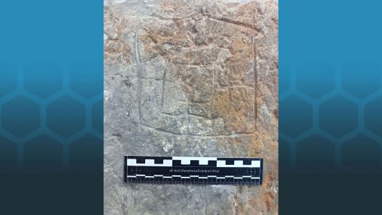 An ancient Nine Men's Morris or Mill board, discovered and photographed by archaeologist Tomasz Olszacki, carved into a sandstone block, with a small ruler demonstrating scale