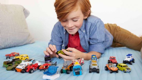 Best Matchbox cars, marketing photograph by Mattel - a red-headed child plays with diecast toy cars on a bed