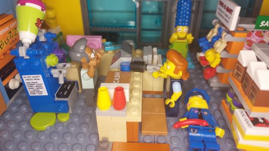 Lego Simpsons Kwik-E-Mart review image show a scene in which Snake tries to rob the store while Chief Wiggum lies on the floor, Apu raises his hands, and Marge looks on in fear.