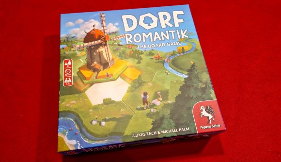 Dorfromantik Board Game review - author photo showing the game's box front art, with a pretty village, wood, and river