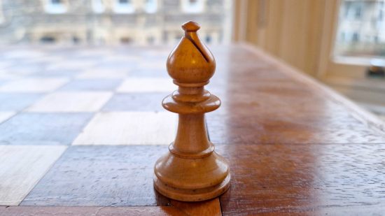 How to play Chess guide - Wargamer original photo showing a white bishop piece on a wooden chessboard