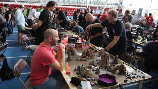 London GT Warhammer 40k tournament - two gamers, one in a chair, one standing, play opposite one another on a low gaming table