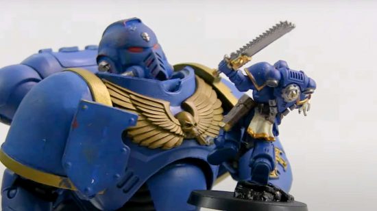 An action figure of a Warhammer 40k Space Marine, holding a Warhammer 40k Space Marine miniature, both in the blue and gold livery of the Ultramarines