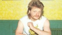 White Dwarf photograph of Warhammer co-creator Bryan Ansell in the 80s,posed with his army, in a sleeveless t-shirt with a mullet and moustache