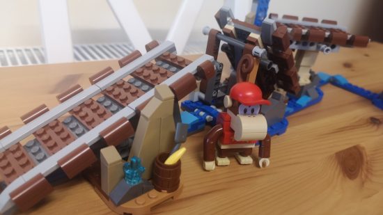 Lego Donkey Kong: Diddy Kong's Mine Cart Ride review image showing Diddy standing near some tracks beside a barrel containing a shovel and a banana.