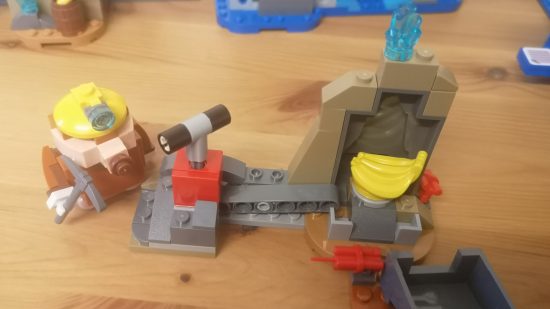Lego Donkey Kong: Diddy Kong's Mine Cart Ride review image showing a mole miner near an exploded rock with a banana inside.