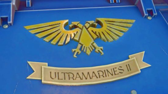 Warhammer 40k Power Wash Simulator DLC release date - a gold two headed eagle 'Aquila' Icon on a blue tank plate, above an honor scroll which reads 'Ultramarines II'