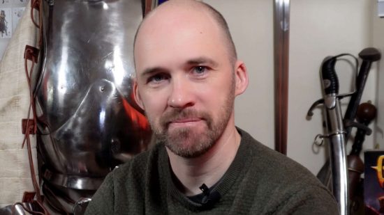Ex-Warhammer TV presenter Chris 'Peachy' Peach, a bald white man with a short beard, wearing a grey sweater