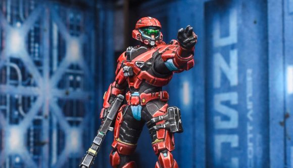 A red-armored Spartan miniature from the upcoming Halo Flashpoint wargame points towards the camera
