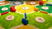 Catan board game deals on Amazon - Catan Studio promotional image showing part of a Catan board set up to start play, with settlements, roads, and dice