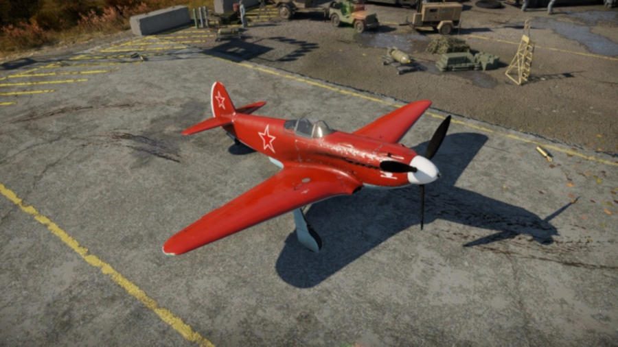 A small and bright red War Thunder plane sitting stationary on tarmac with a propeller on its nose