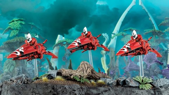 Warhammer 40k Eldar jet bike riders painted red, arranged amidst tropical, rocky terrain.