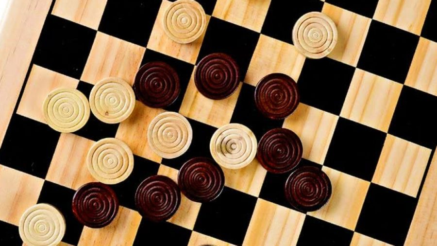 How to play checkers - a wooden checkerboard seen from above, with a mix of light and dark checker pieces scattered on top