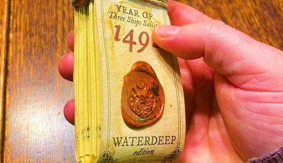 A hand-made folding almanack held in someone's hand - it shows a red wax seal and the text "waterdeep edition" on the front, with the year of the almanack partially concealed by the holder's thumb.